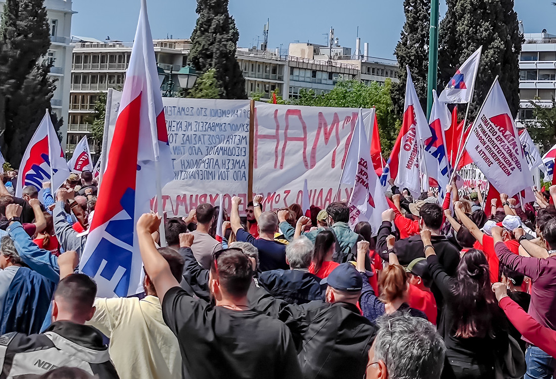 A large crowd of workers marches with flags, banners, and raised fists during a May Day rally in Athens, expressing solidarity and support for labor rights.