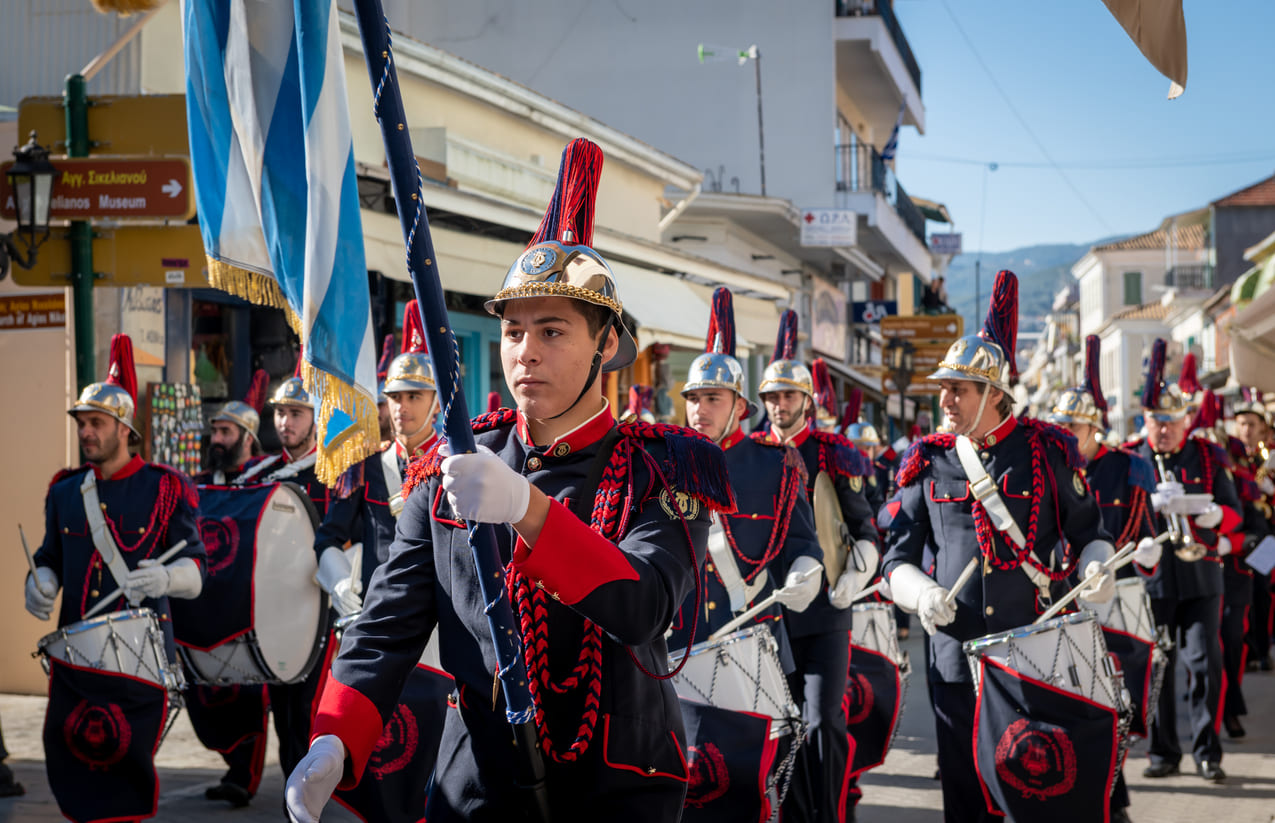 Uniformed drummers and flag bearers parade through a Greek town, honoring Ochi Day with patriotic precision and pride.