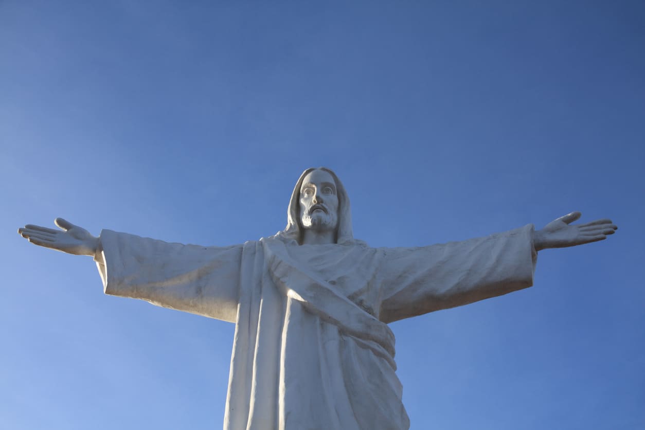 Statue of Jesus Christ with outstretched arms against a clear blue sky, symbolizing peace and divine blessings.