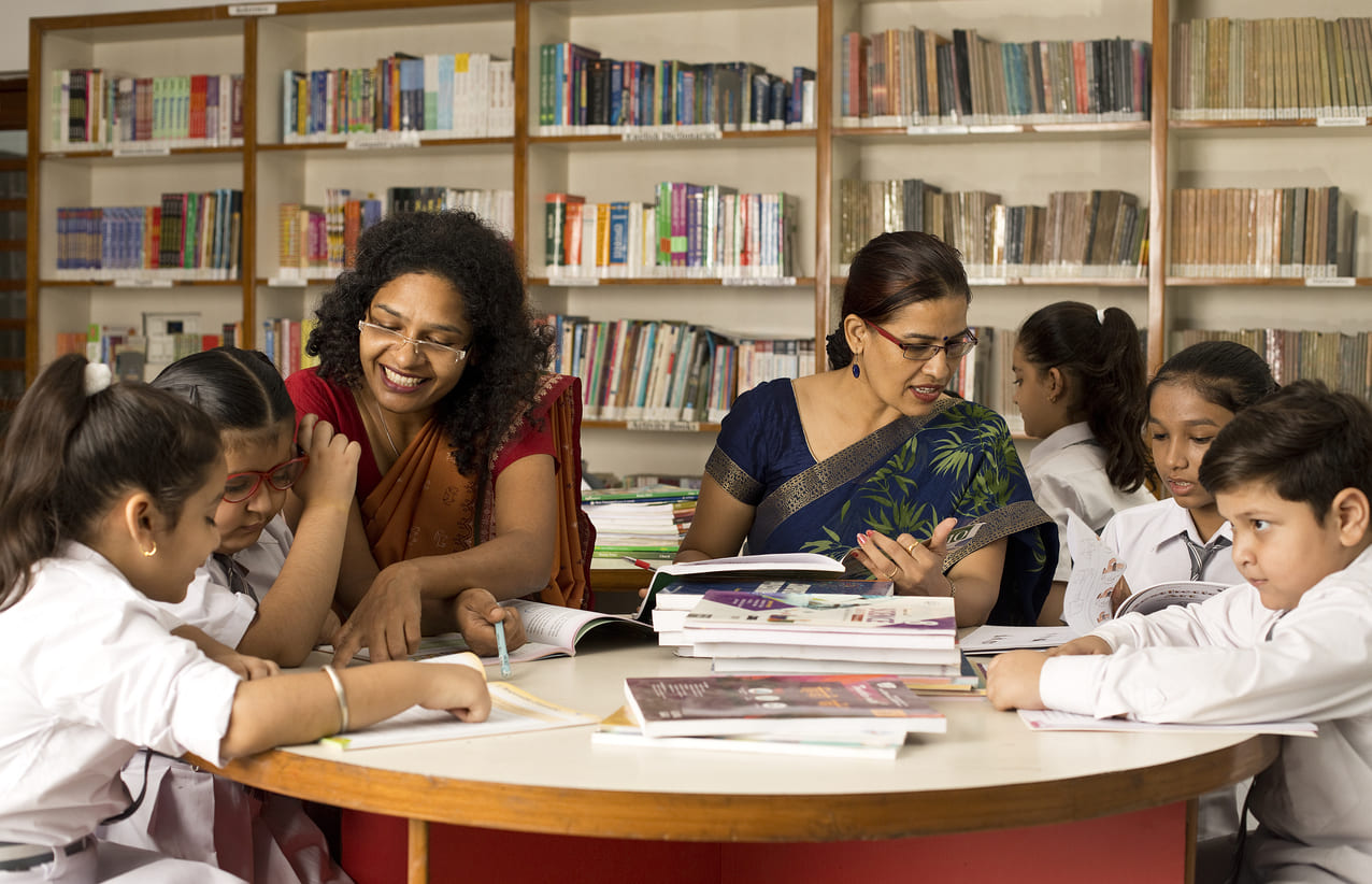 Teachers guiding students in a library, symbolizing the mentorship and knowledge celebrated on Guru Purnima.