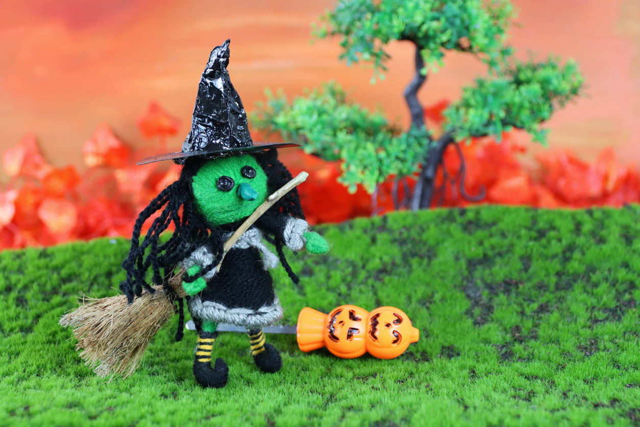 A whimsical witch figurine with a broom, set in a colorful, festive Halloween scene.