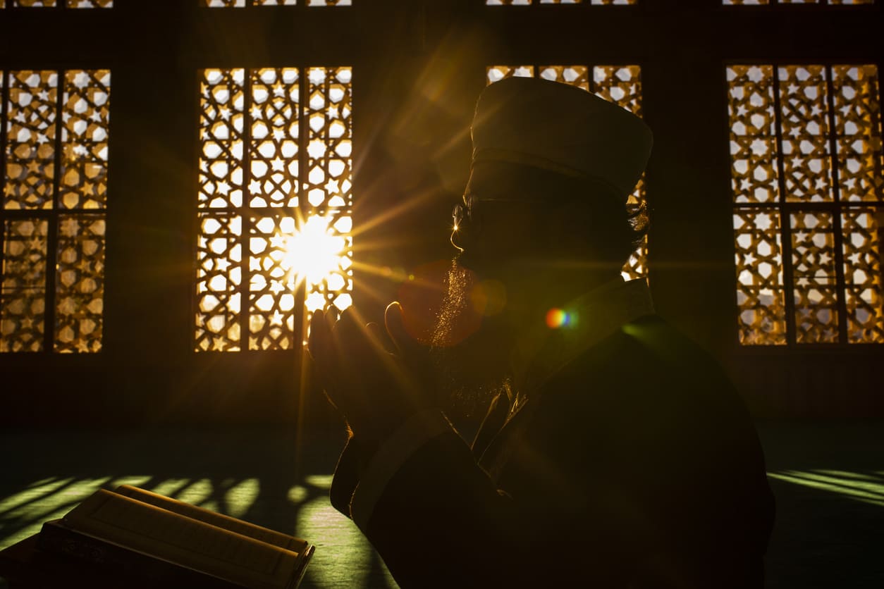 A worshiper immersed in prayer as sunlight streams through intricate lattice windows, reflecting serenity and devotion.