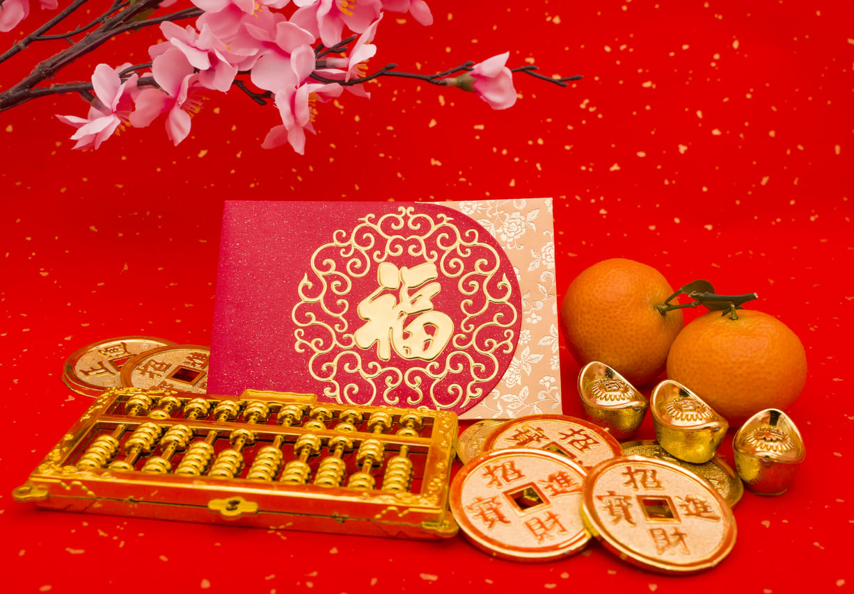 New Year decorations featuring red envelopes, gold ingots, coins, an abacus, oranges, and cherry blossoms, symbolizing prosperity and good fortune.