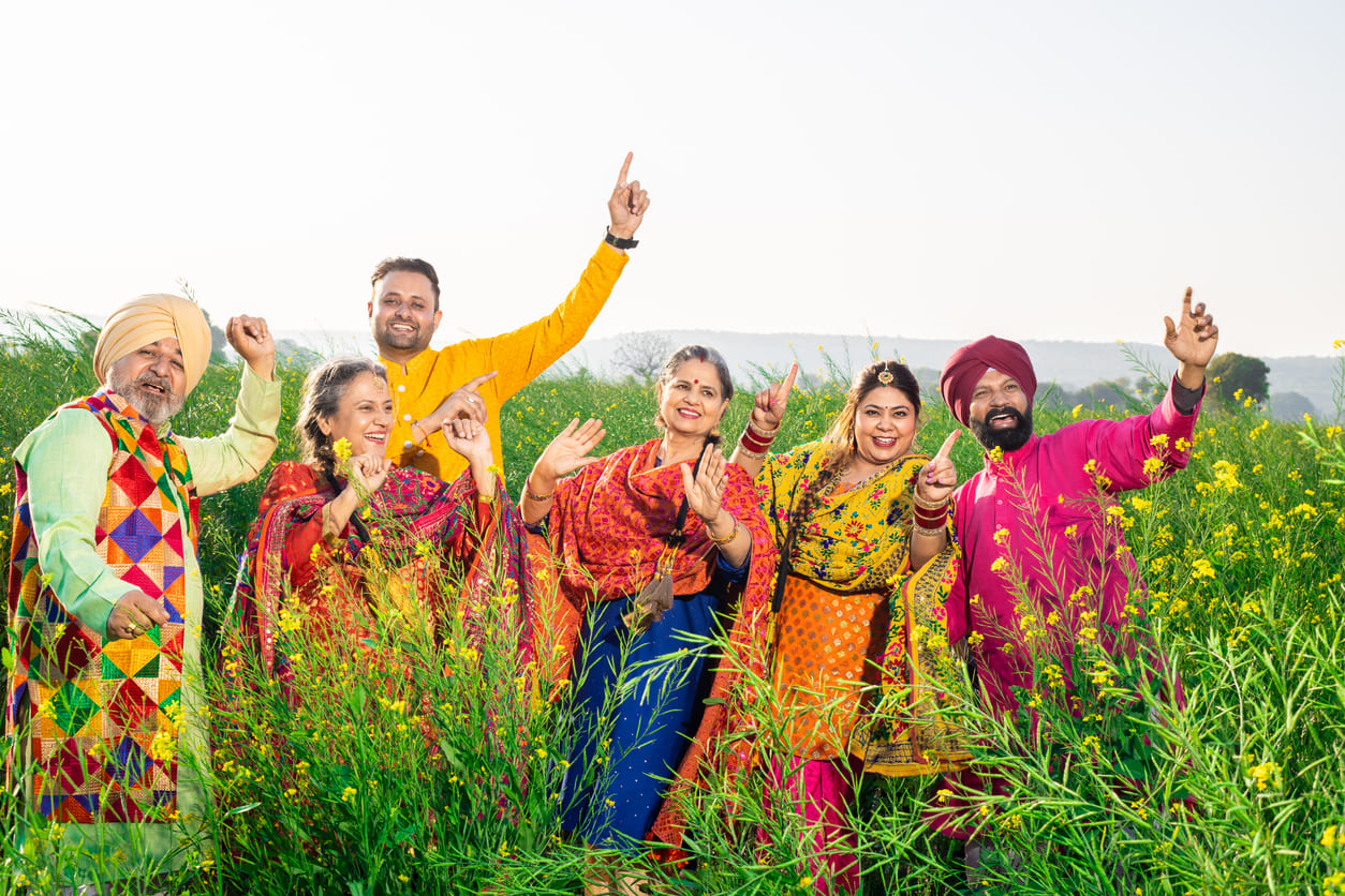 A joyful group dressed in vibrant traditional Punjabi attire, celebrating Vaisakhi amidst blooming mustard fields.