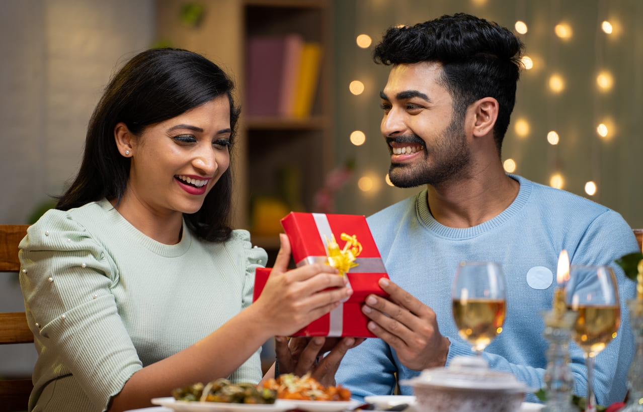 A happy couple exchanging a gift while enjoying a cozy and romantic dinner.