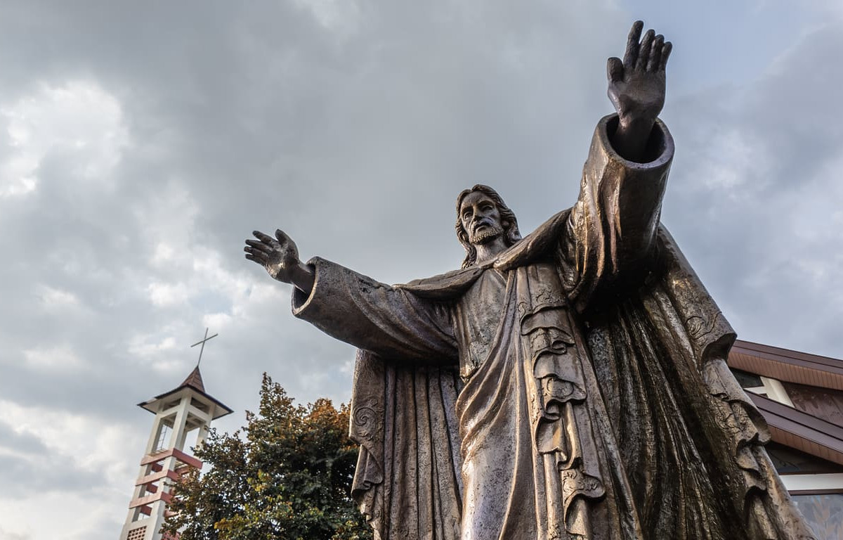A bronze statue of Jesus with outstretched arms stands before a church, reflecting the spirit of Ascension Day of Jesus Christ in Indonesia.