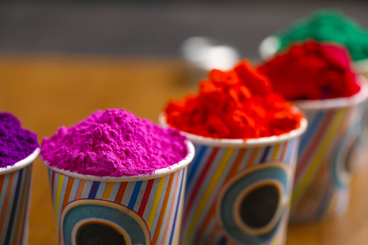 Vibrant cups filled with bright colors, neatly arranged in a row, capturing the festive spirit of Holi celebrations.