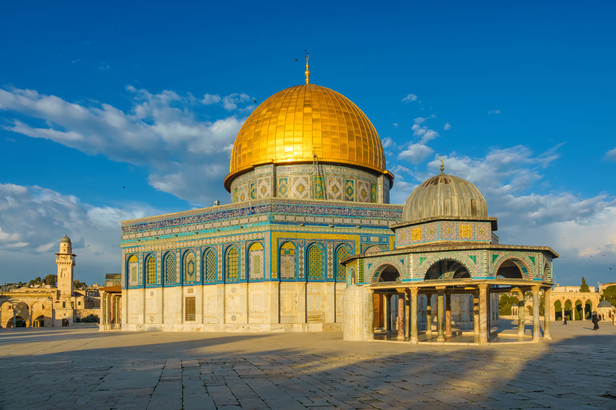 A stunning view of the Dome of the Rock in Jerusalem, with its golden dome and intricate tilework under a clear blue sky.