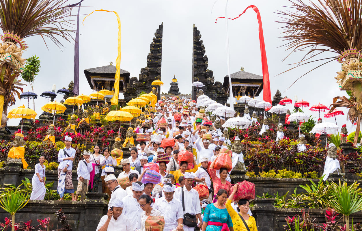 Balinese Hindus in traditional attire ascending the steps of Pura Besakih, carrying offerings during a vibrant temple ceremony.