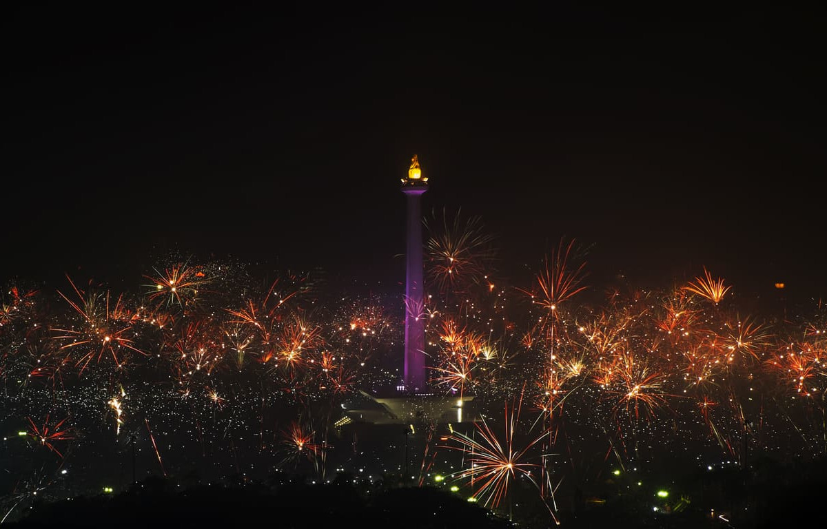A vibrant night scene with fireworks bursting around Jakarta's National Monument, celebrating the arrival of the New Year.