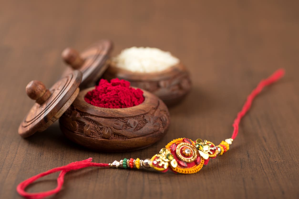 A decorative rakhi placed beside wooden containers of kumkum and rice, symbolizing the traditional rituals of Raksha Bandhan.