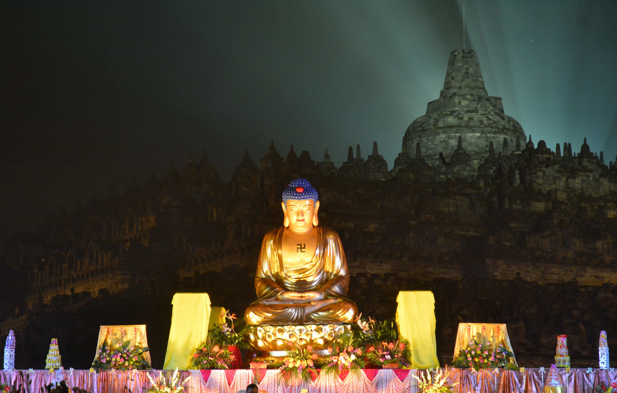 A beautifully illuminated Buddha statue set against the backdrop of Borobudur Temple during the serene night-time Waisak Day celebrations.