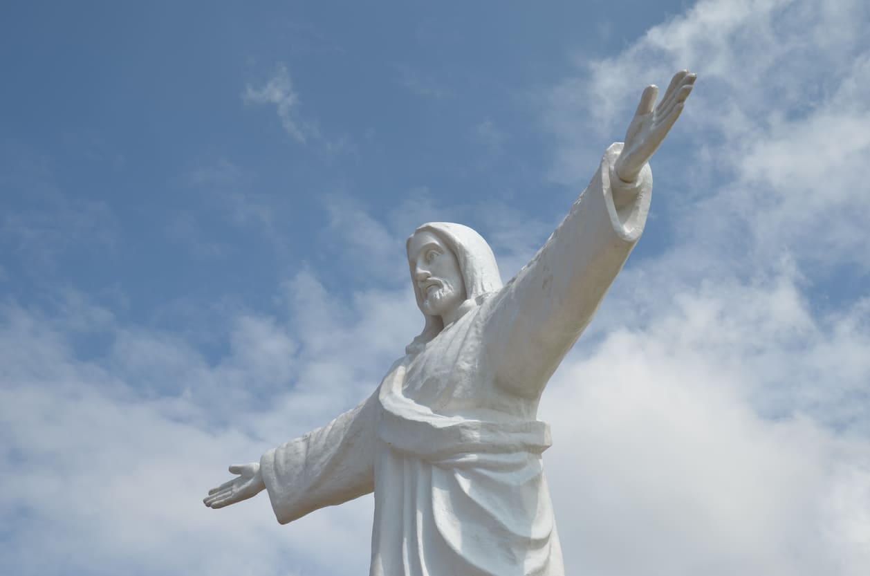 A statue of Jesus Christ with outstretched arms against a bright sky, symbolizing His ascension into heaven.