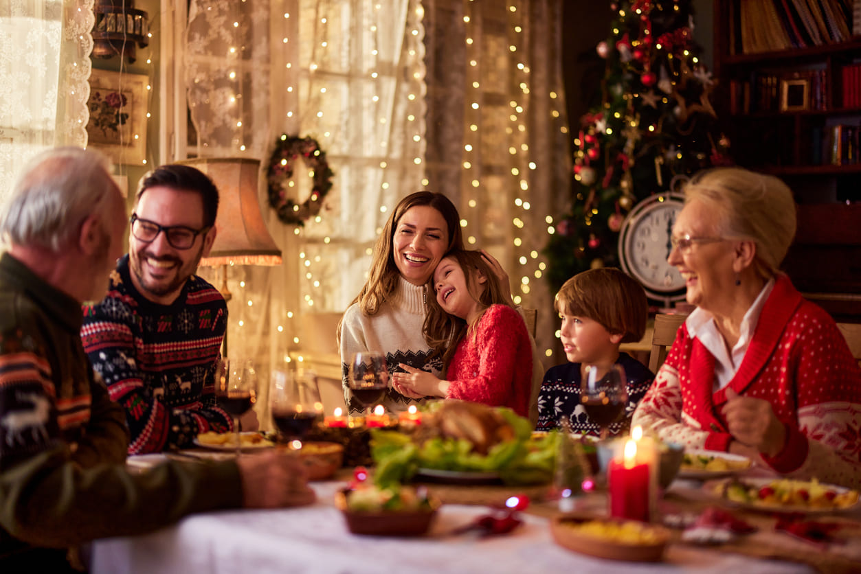 A joyful family gathered around a festive dinner table, surrounded by Christmas lights, decorations, and a beautifully lit tree.