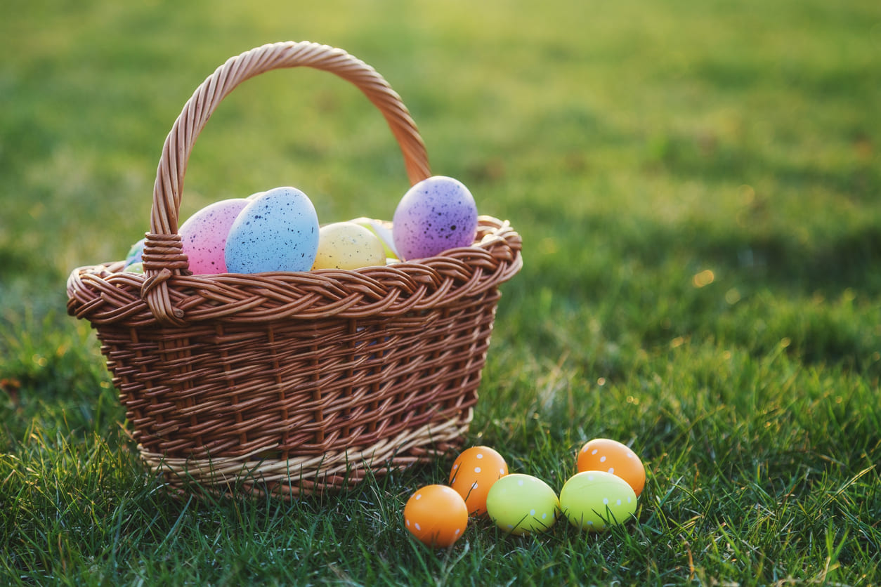 A wicker basket filled with vibrant Easter eggs resting on lush green grass, capturing the essence of a festive egg hunt.