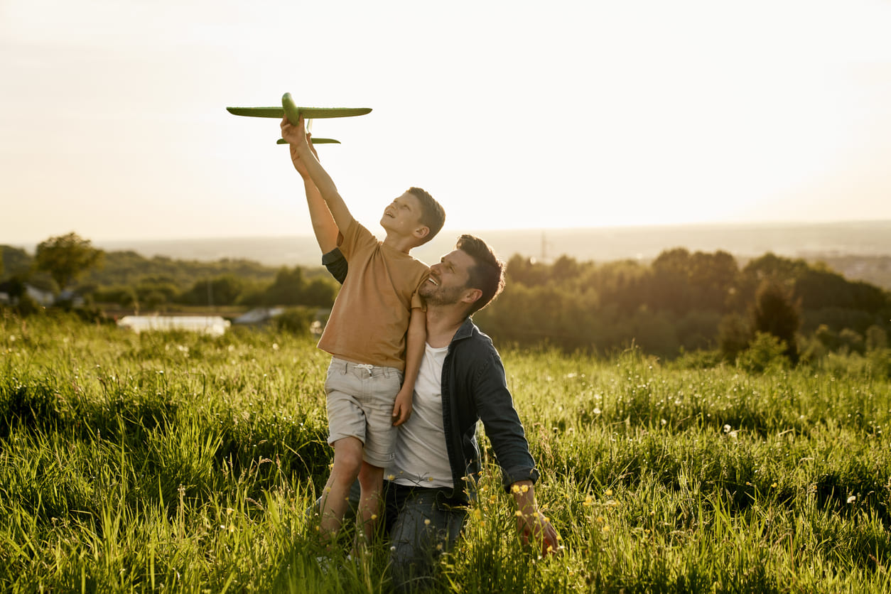 A father and son enjoying a sunny outdoor moment, with the boy holding a toy plane, symbolizing joy and connection.