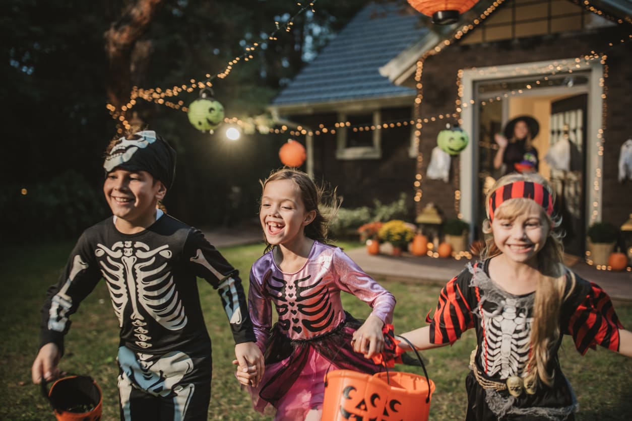 Excited children in Halloween costumes holding treat buckets, enjoying trick-or-treating in a festively decorated yard.