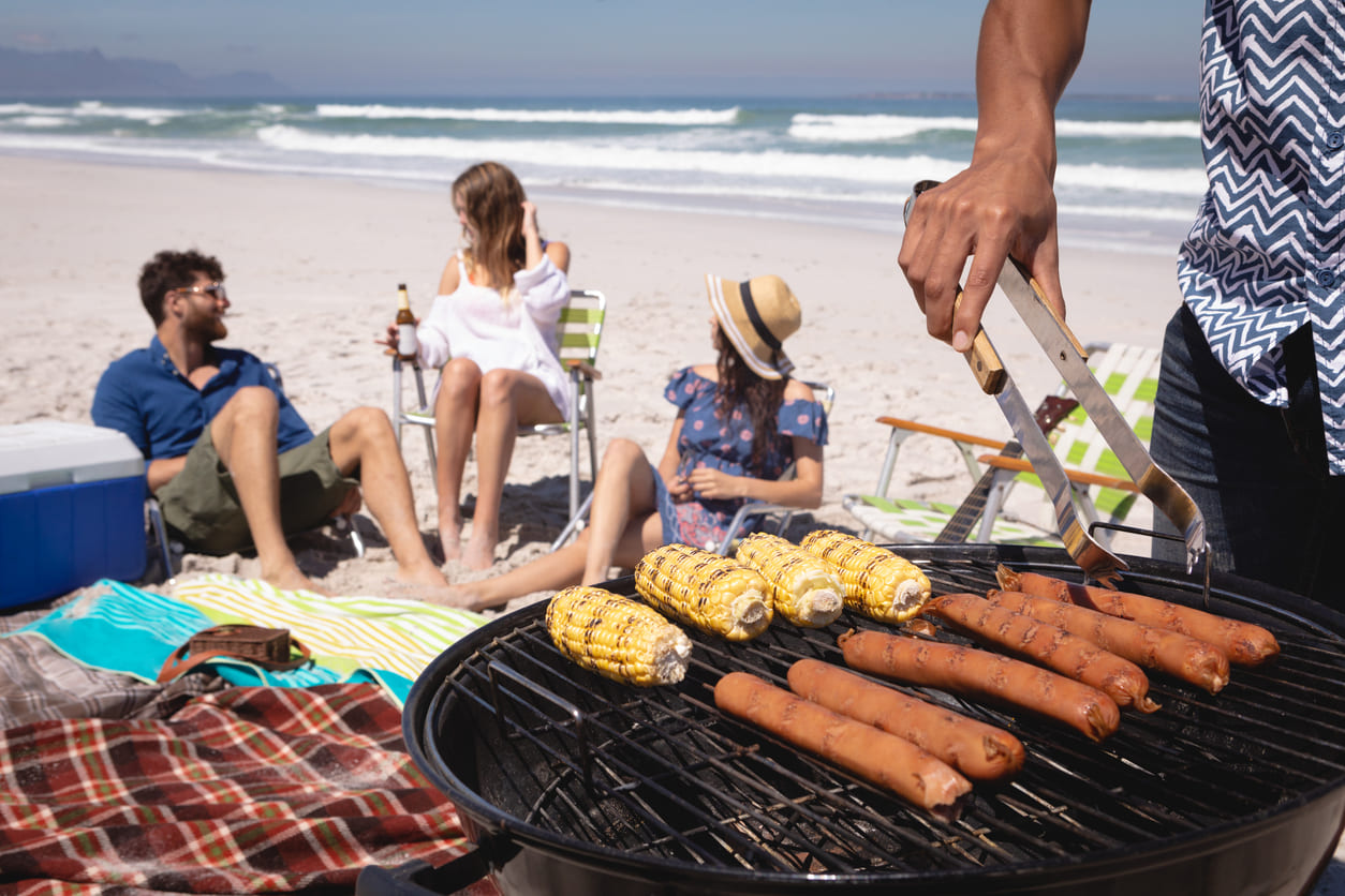 A group of friends relaxing on a sunny beach with a barbecue, enjoying food and the carefree atmosphere.