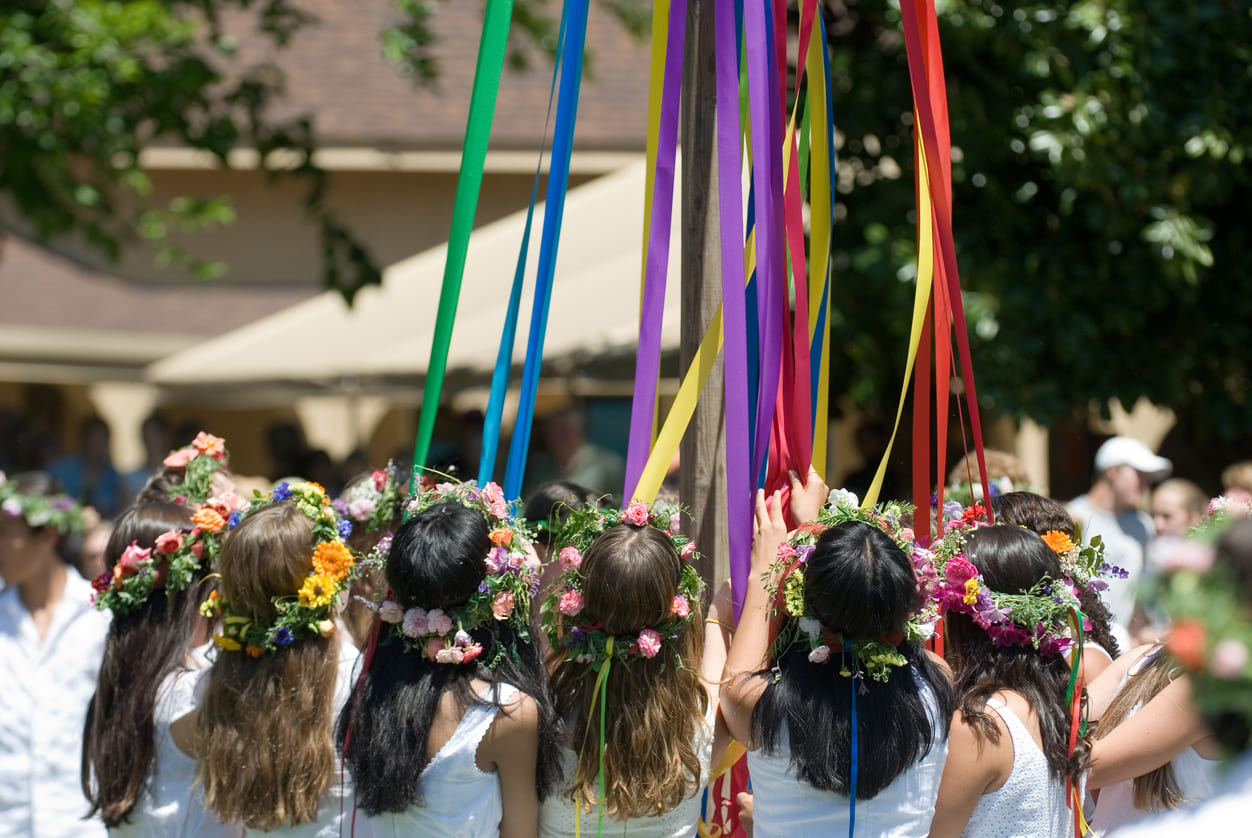 Young children with flower crowns dancing around a colorful maypole, celebrating the joyous traditions of May Day.