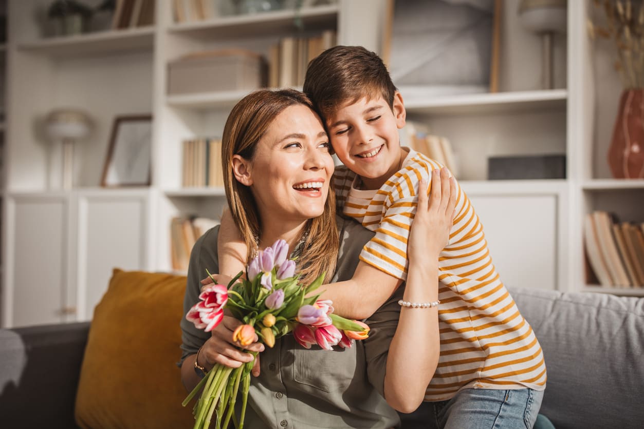 A joyful mother and child sharing a loving embrace, with the mother holding a bouquet of colorful flowers.