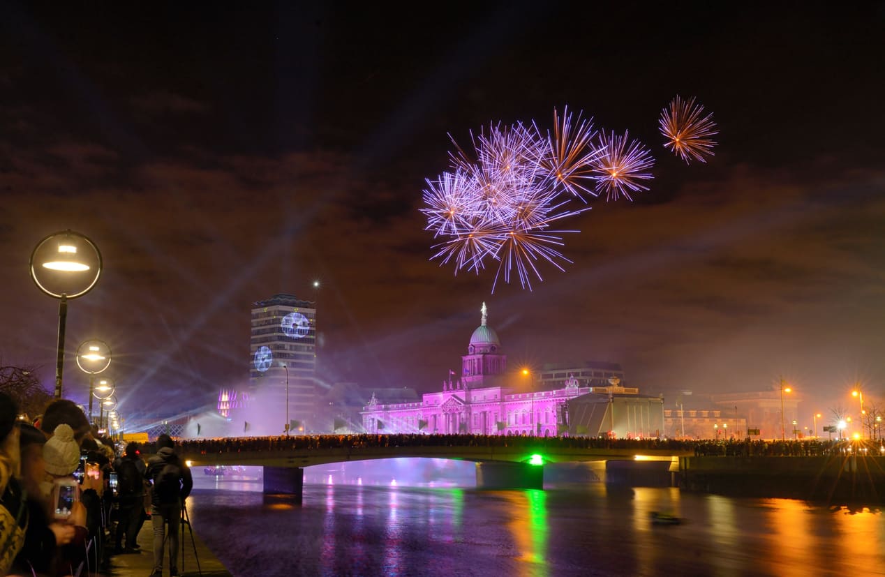 A vibrant display of fireworks illuminates the night sky over Dublin's Custom House, reflecting festive New Year's celebrations.