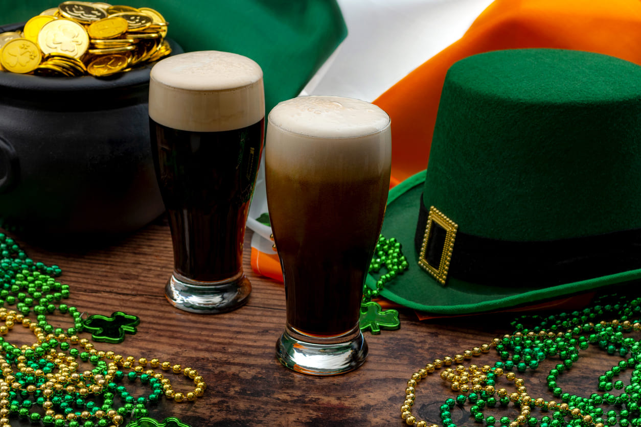 Two pints of stout, a leprechaun hat, gold coins, and festive beads, symbolizing the vibrant spirit of St. Patrick's Day.