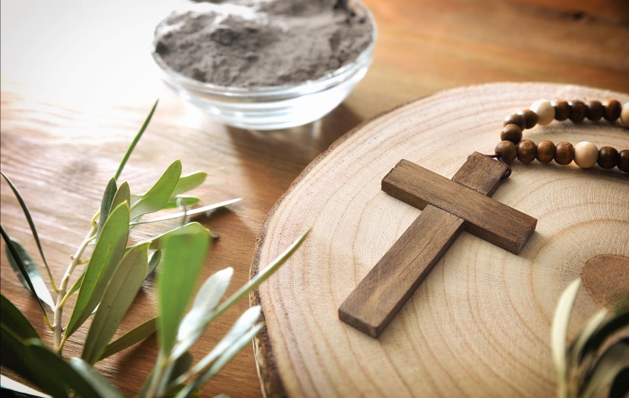 Ash Wednesday symbols: ashes, a wooden cross, olive branches, and prayer beads, representing faith and repentance.