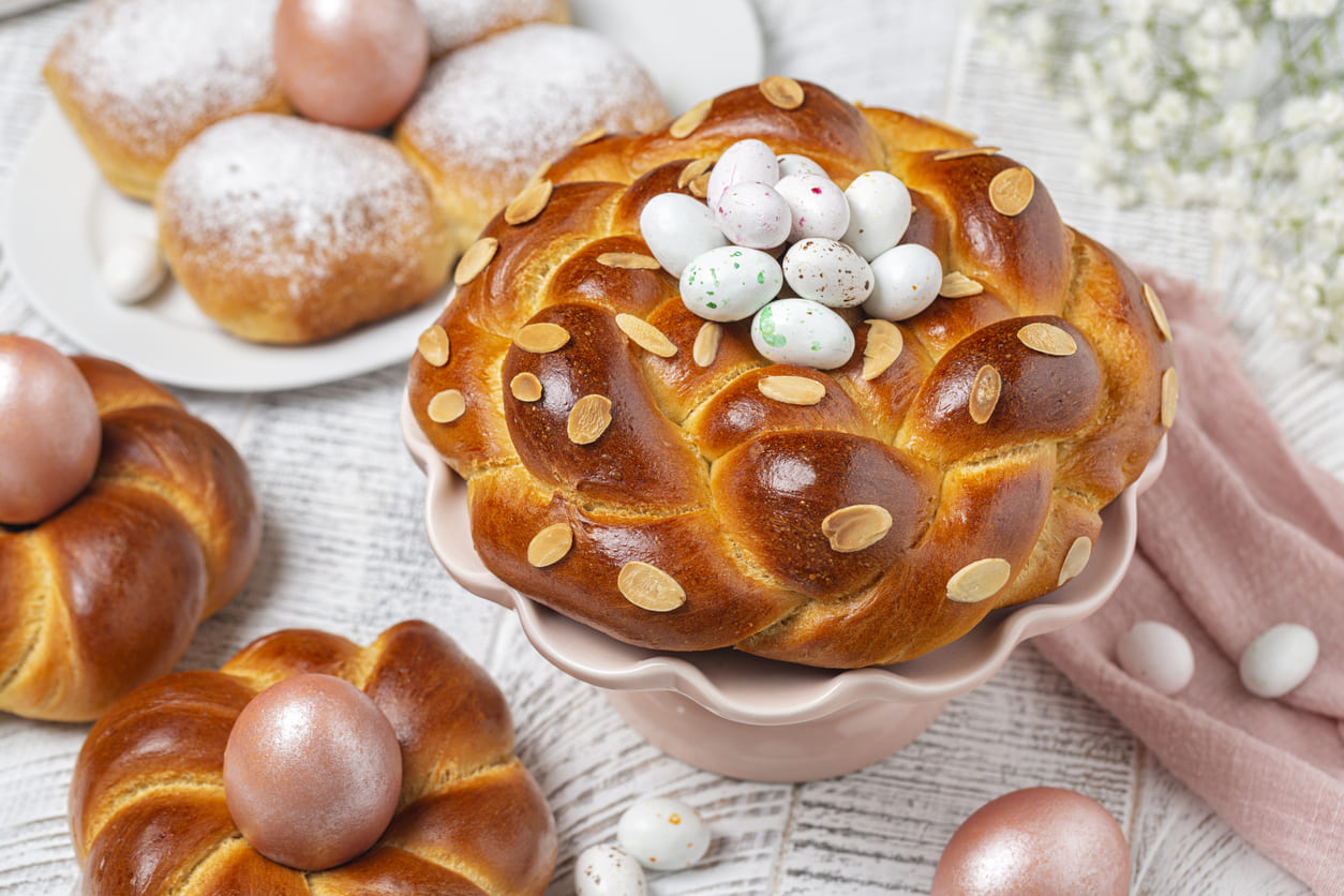 Italian-style braided buns and a festive bread centerpiece, decorated with almonds and colorful Easter eggs.