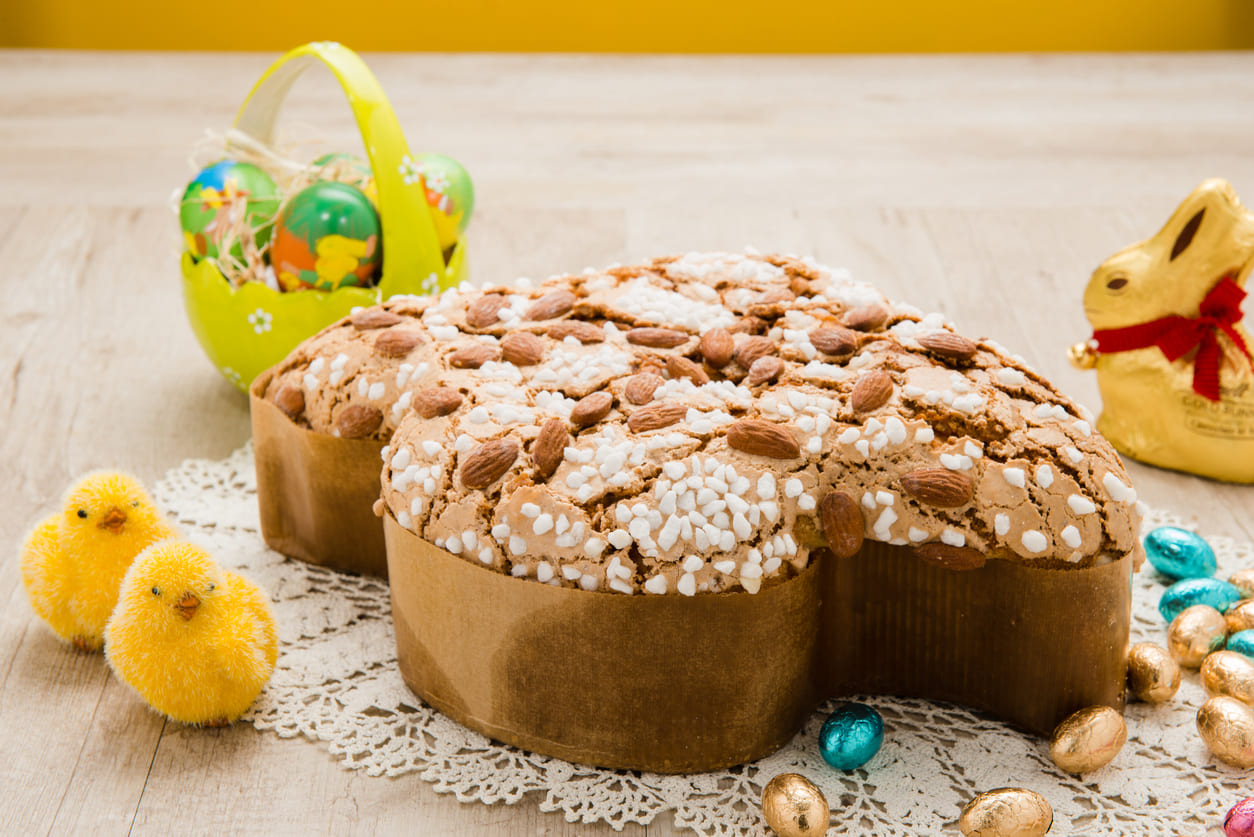 Traditional Italian colomba cake with almonds, surrounded by Easter eggs, chicks, and a chocolate bunny.