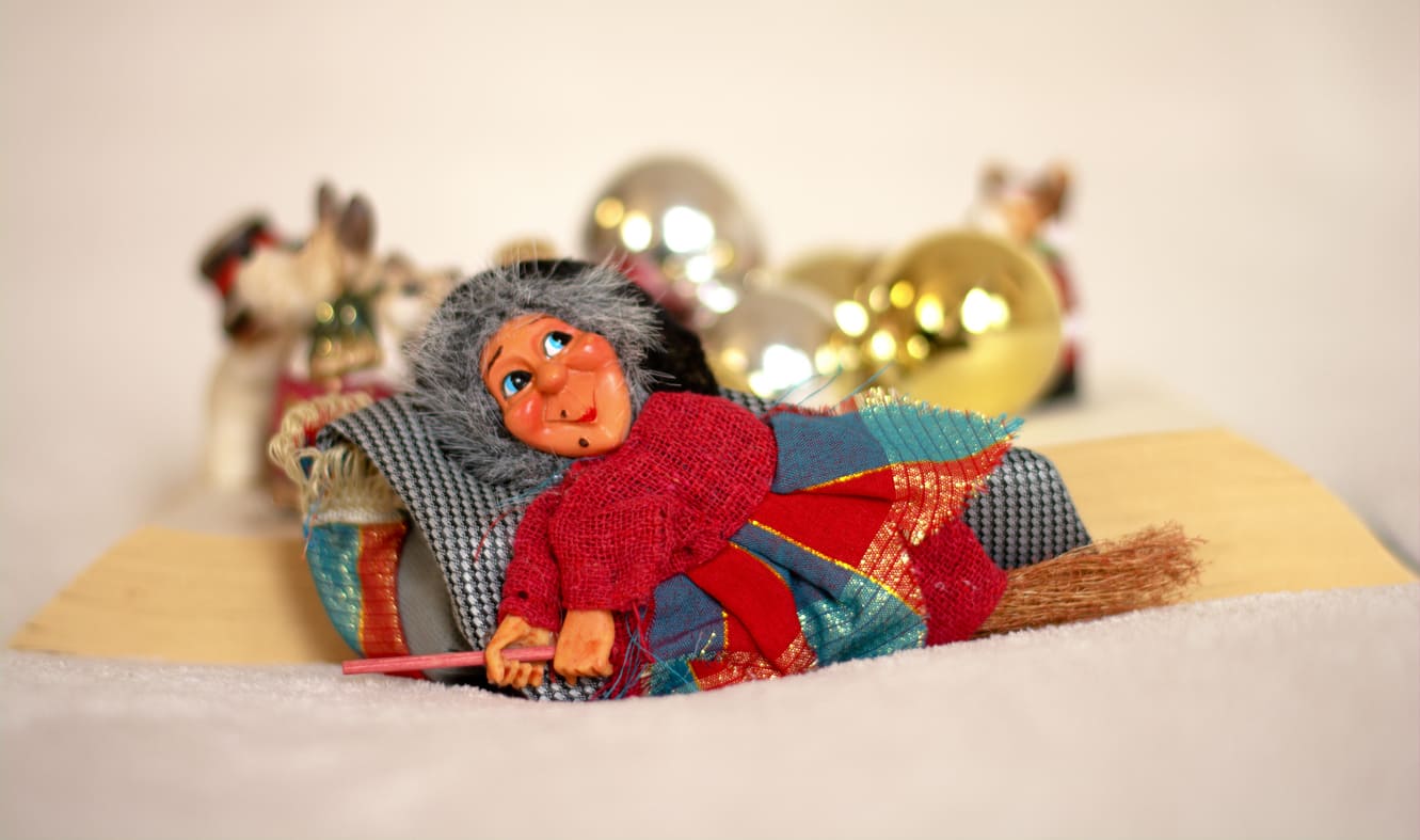 A cheerful La Befana figurine, dressed in colorful fabric, lies among festive decorations, embodying Italy's Epiphany tradition.