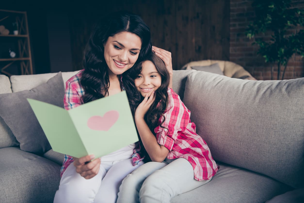 A mother and daughter share a warm moment together while reading a heartfelt card.