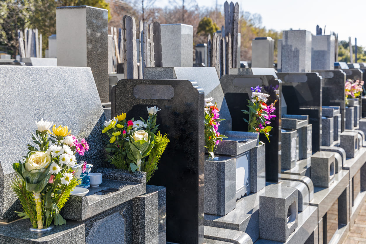 Rows of polished gravestones are lined with colorful flower offerings, bathed in sunlight, creating a serene and respectful atmosphere.