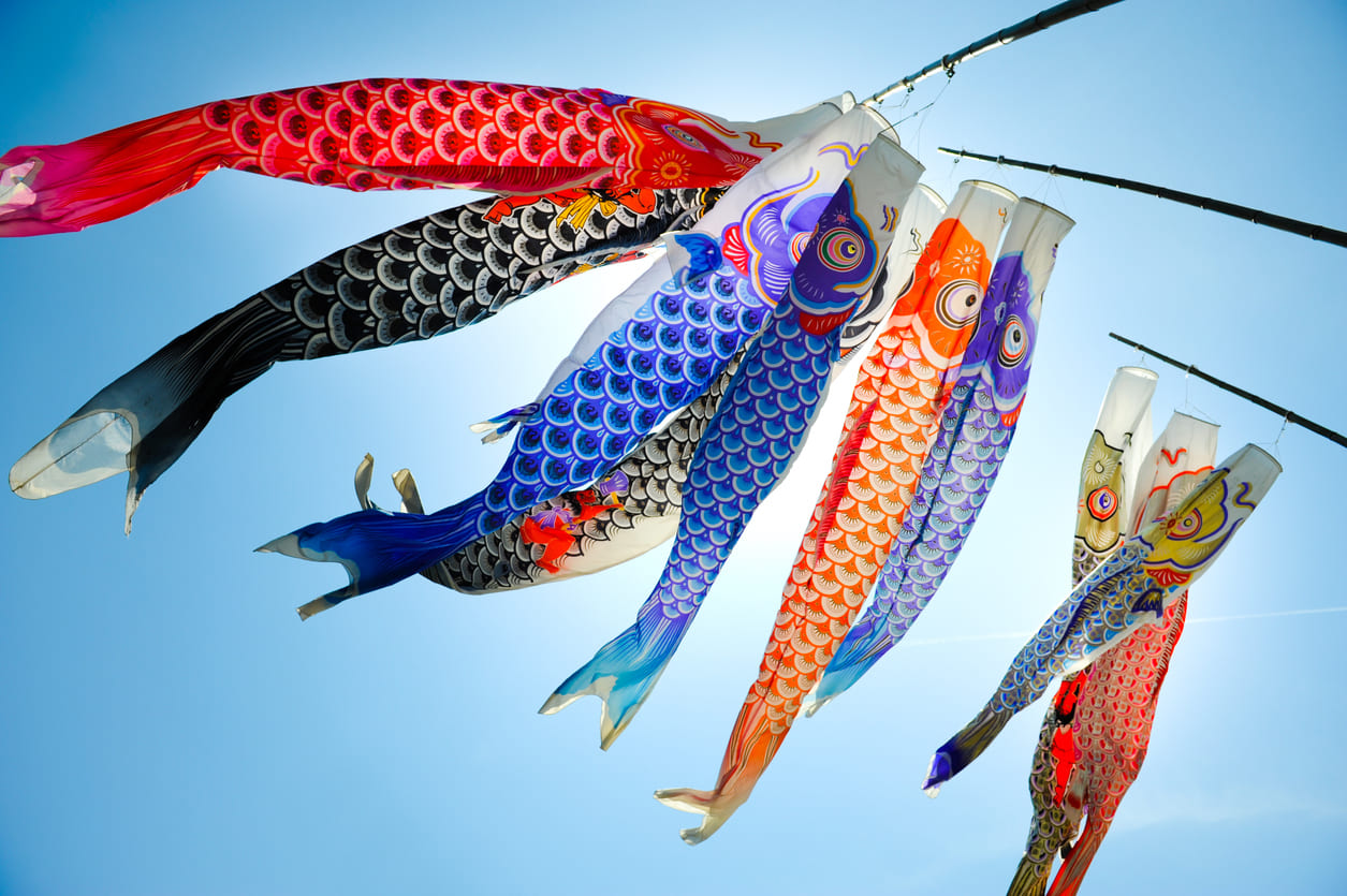 A cluster of brightly colored carp-shaped streamers sways against a clear blue sky, creating a festive and uplifting scene.