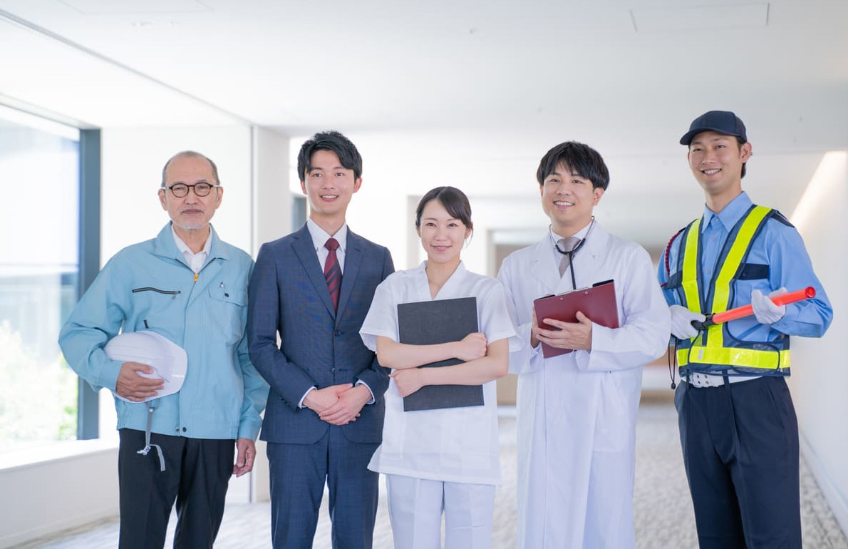 A group of professionals from various fields, including healthcare, construction, and business, standing together in a bright hallway, symbolizing unity and respect for labor.