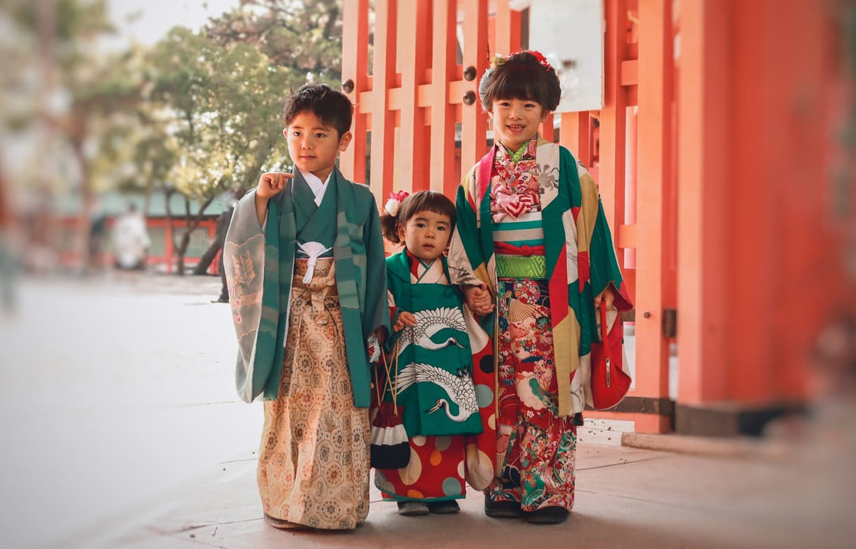 Three young children in elegant kimono standing near a shrine, capturing the tradition and joy of Shichi-Go-San.