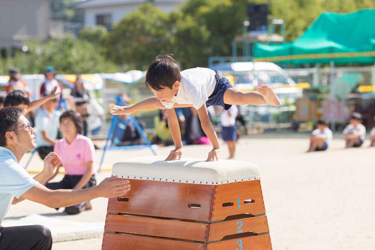 A student mid-air during a vaulting activity, guided by a teacher, highlighting the excitement and energy of a school Sports Day.