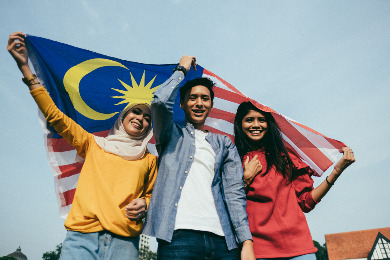 A group of smiling Malaysians holding the national flag, symbolizing national pride and multicultural unity on Malaysia Day.