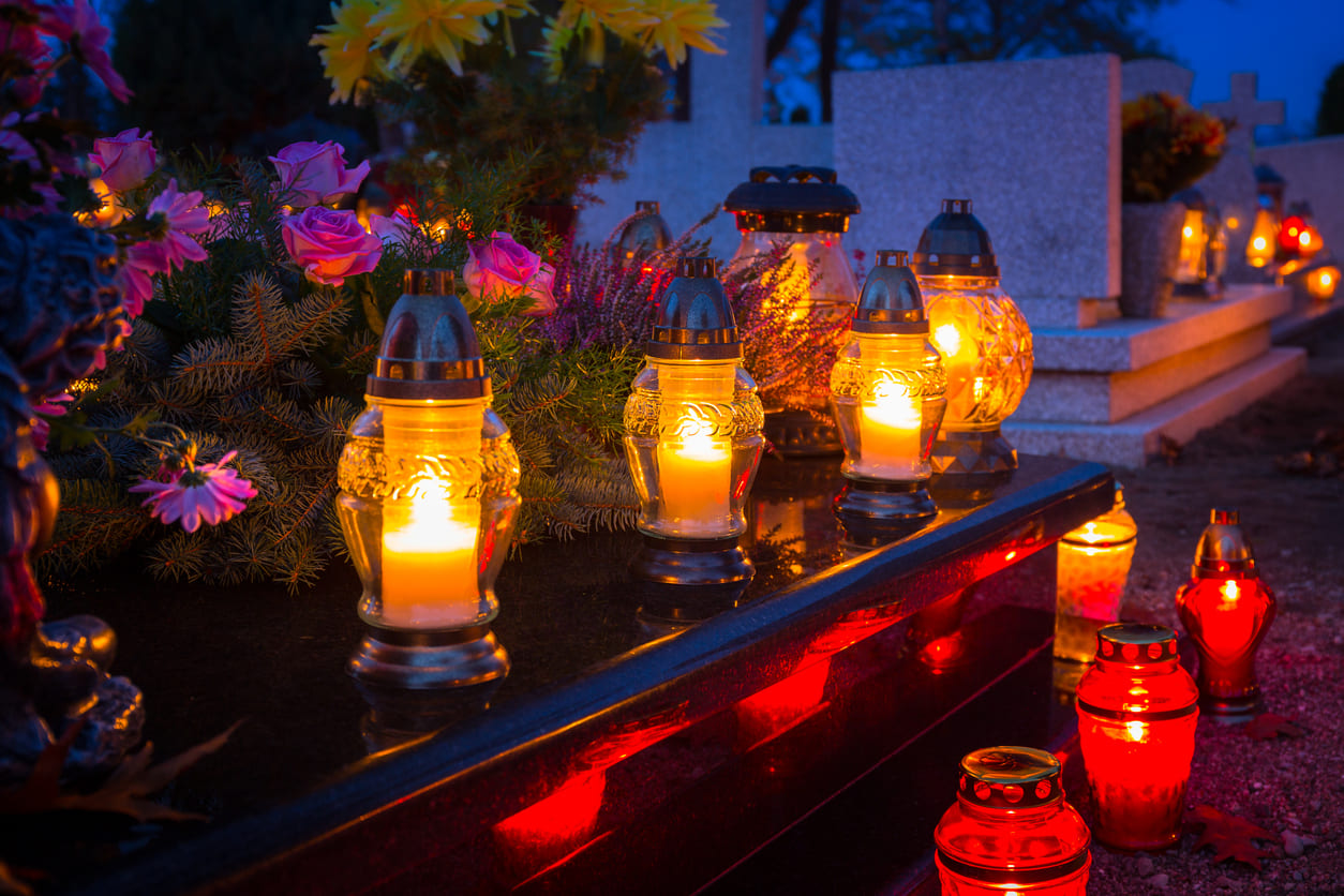 A row of glowing candles and fresh flowers beautifully adorns graves, reflecting love and remembrance on All Saints' Day.