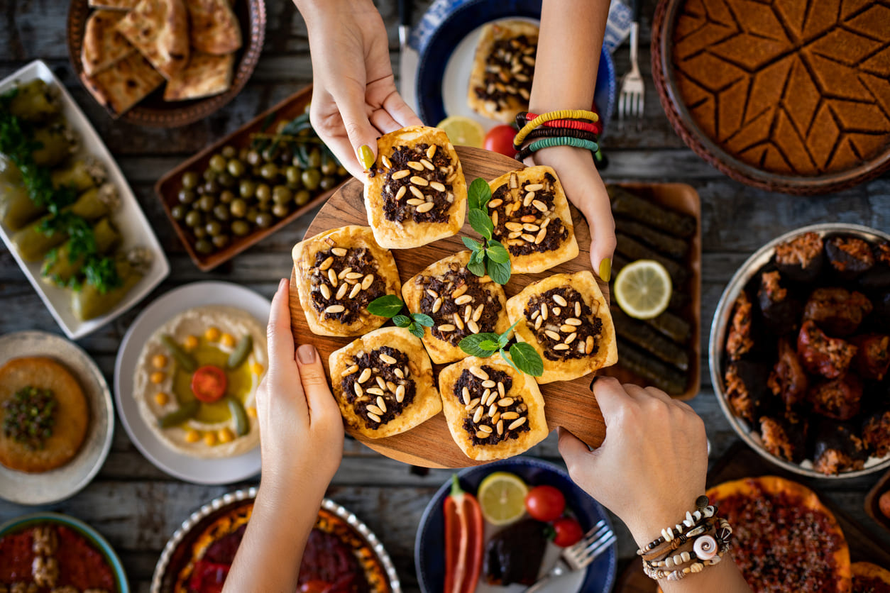 A colourful spread of festive dishes and sweets is shared among hands, capturing the warmth and joy of Eid-ul-Fitr celebrations.