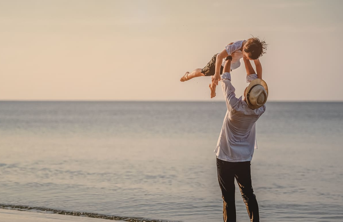 A joyful moment of a father lifting his child by the seaside, capturing the warmth and bond of fatherhood.