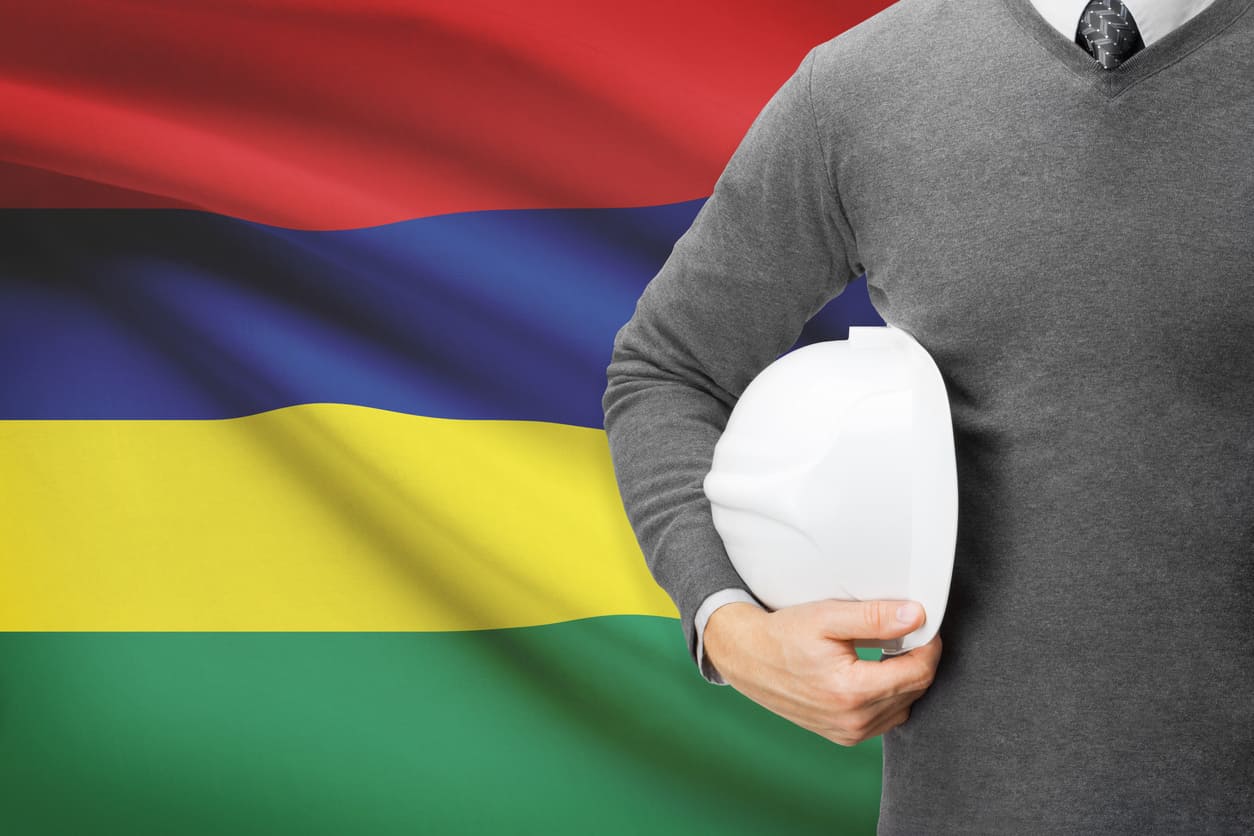 Worker holding a safety helmet against the backdrop of the Mauritius flag, representing labor pride and national unity.