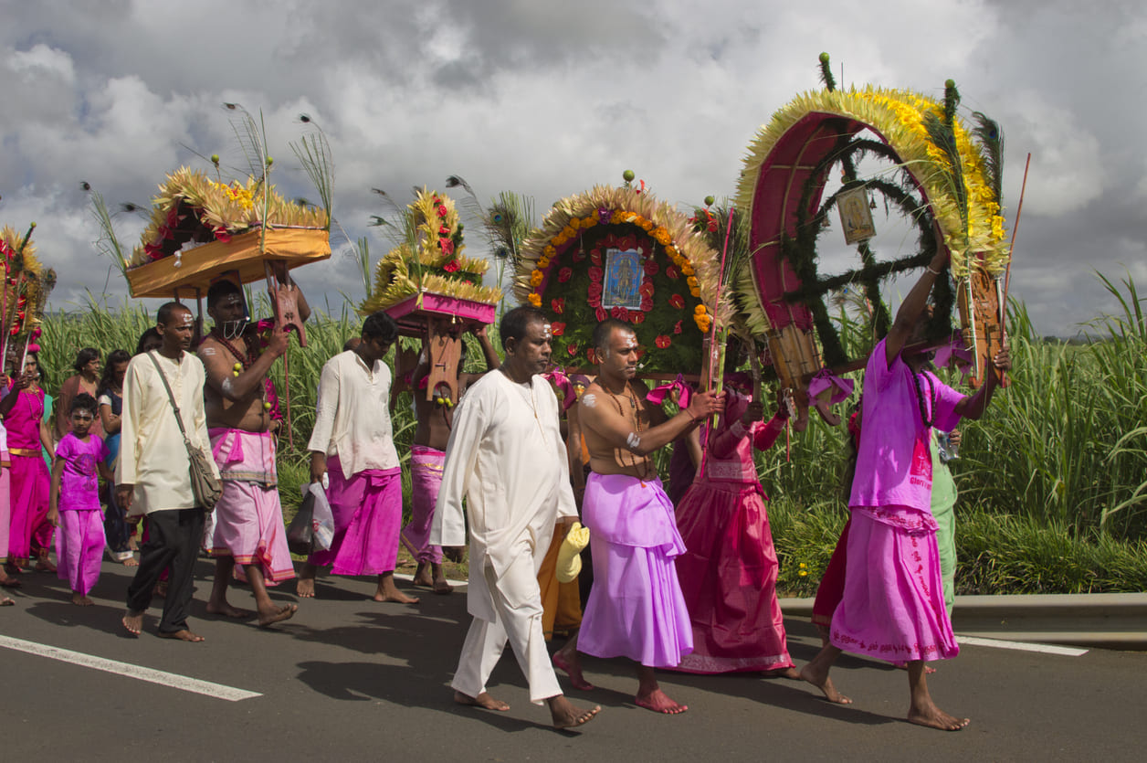 A vibrant street procession of barefoot devotees carrying flower-decorated Cavadees, showcasing deep devotion during Thaipoosam Cavadee in Mauritius.