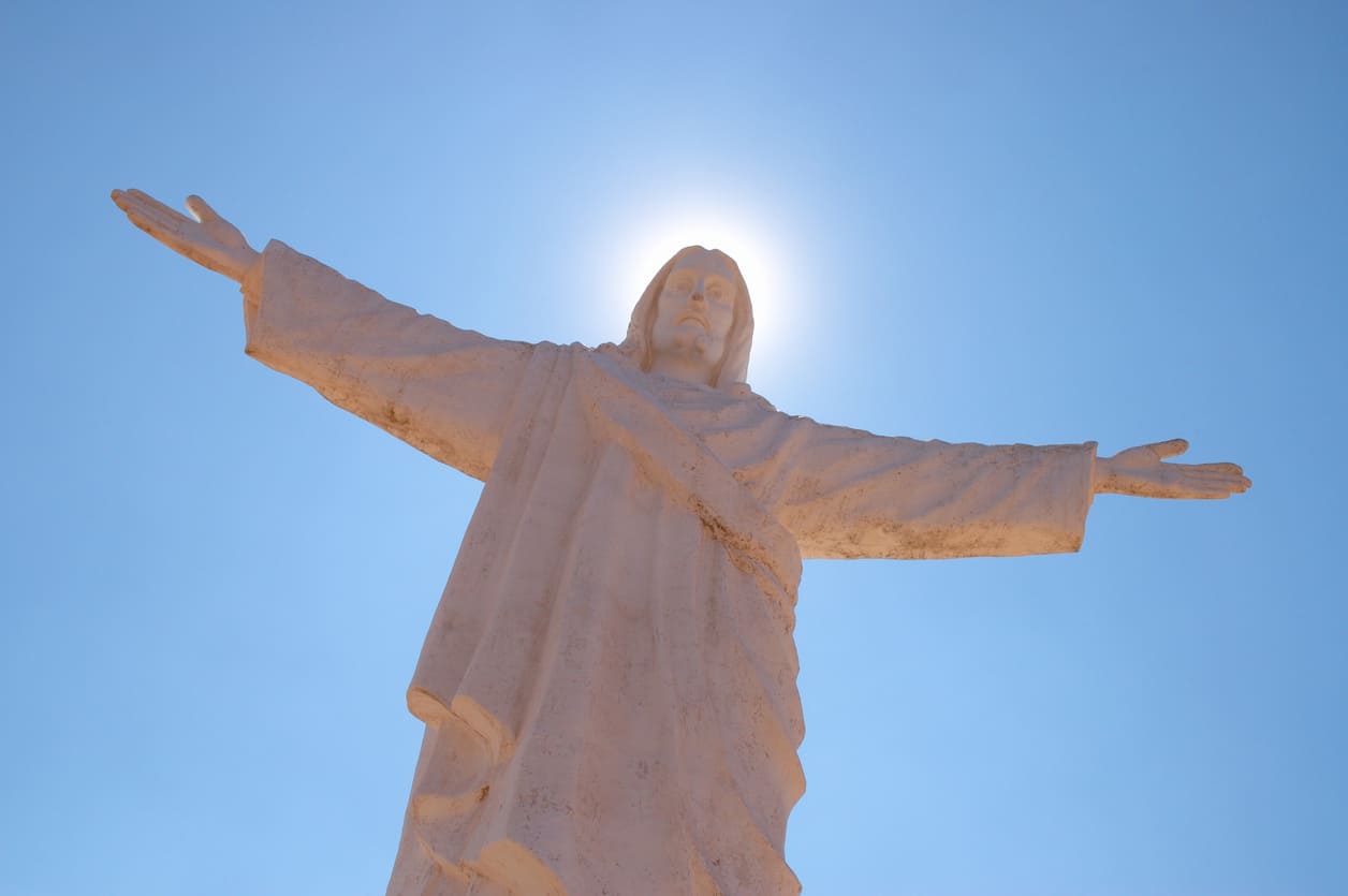 A statue of Christ with open arms, symbolizing hope and ascension, under a radiant blue sky.