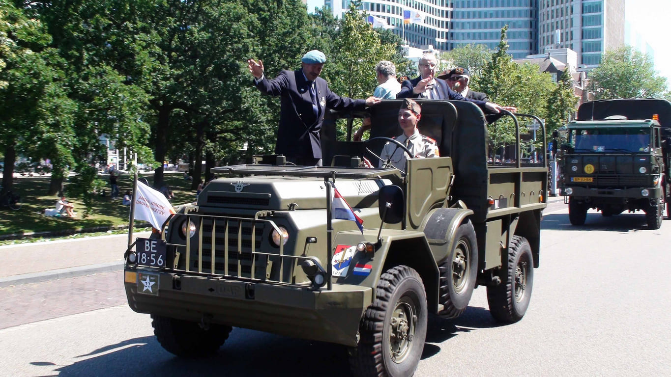 A historic military vehicle carrying veterans parades through a sunny street, symbolizing freedom and remembrance on Liberation Day in the Netherlands.