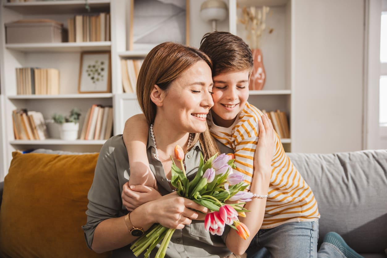 A loving child hugs their mother while presenting a bouquet of tulips, capturing a warm Mother's Day moment.