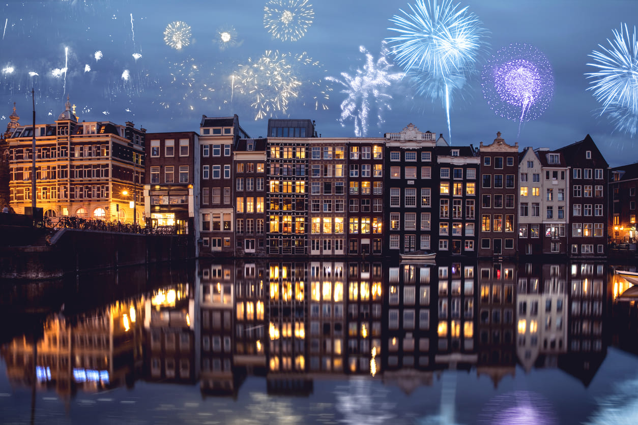 Amsterdam's canal houses glow under vibrant fireworks, celebrating the New Year.