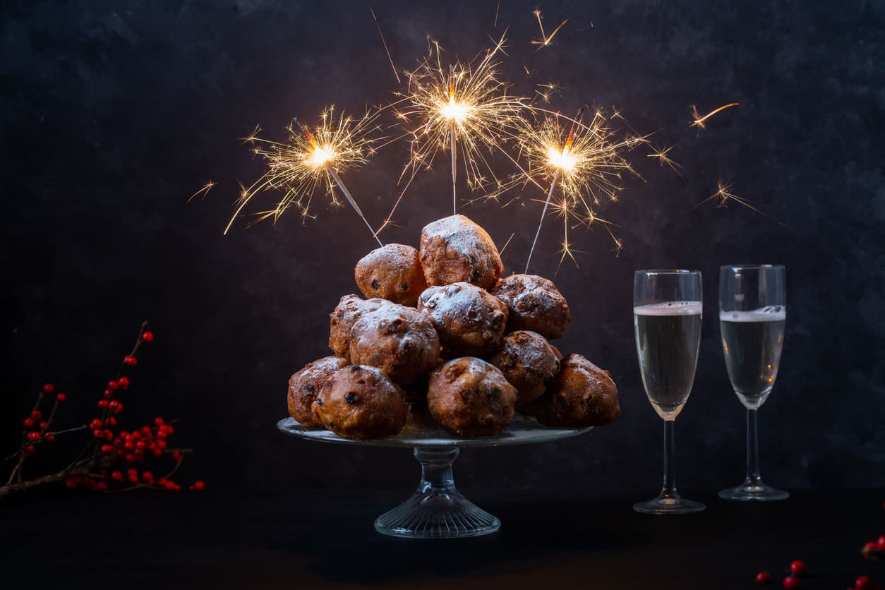 A plate of traditional Dutch oliebollen adorned with sparklers, accompanied by glasses of champagne, celebrating New Year's Eve.