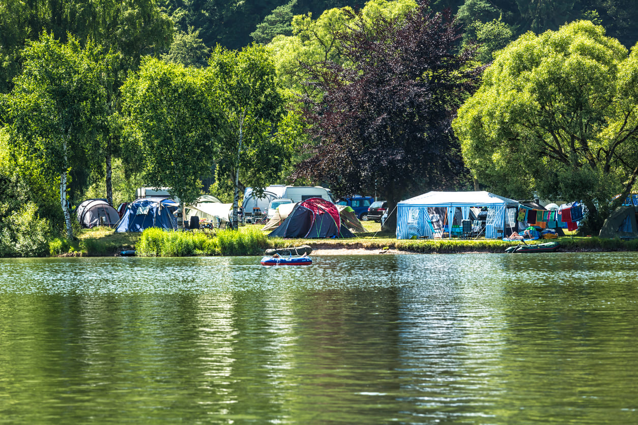 A serene lakeside campsite with tents and vibrant greenery, reflecting relaxation and outdoor leisure.