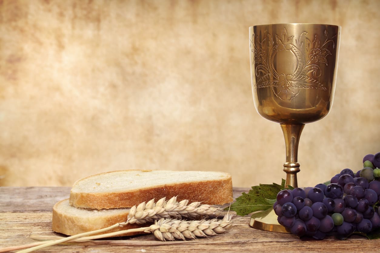 A golden chalice, bread, wheat, and grapes on a wooden surface, symbolizing Christian faith and communion.