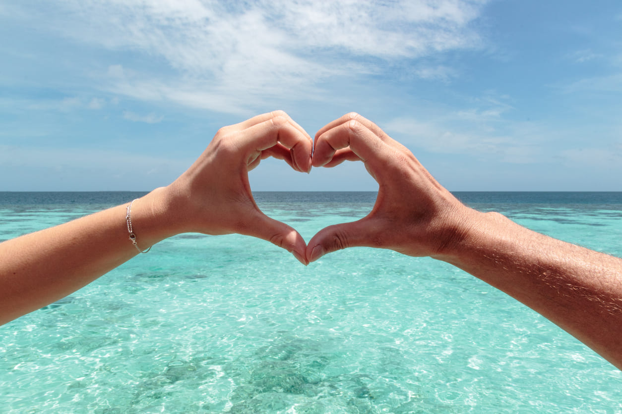 Two hands forming a heart shape over a serene turquoise sea, symbolizing love and unity.